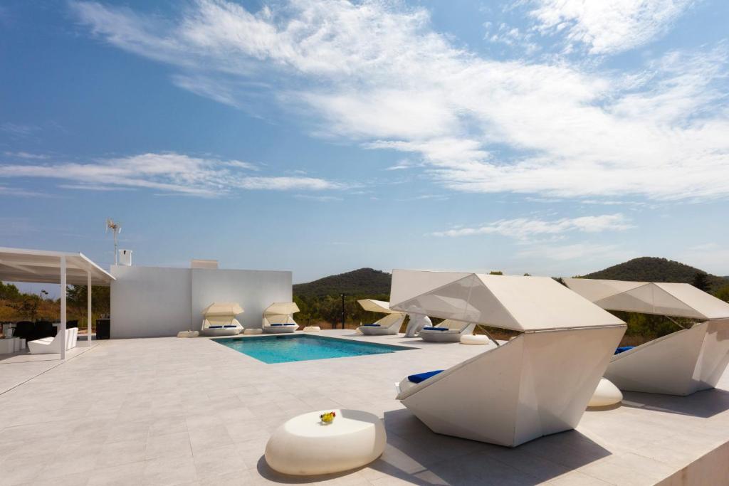 The pool terrace at Villa Boutique Balafi — white geometric parasols, sun loungers and a pool, with the Ibiza hills behind.